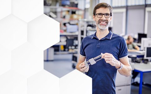 Mann mit Brille steht in Produktionshalle und lächelt
